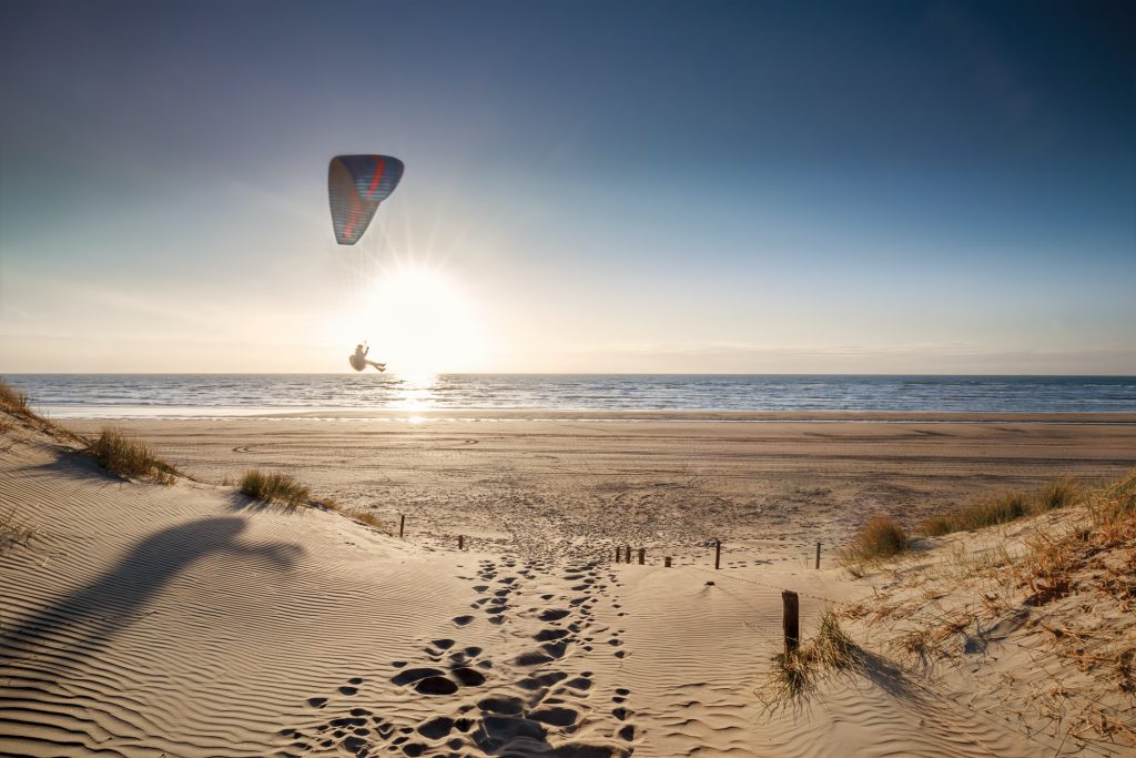 man paragliding on beach at sunset